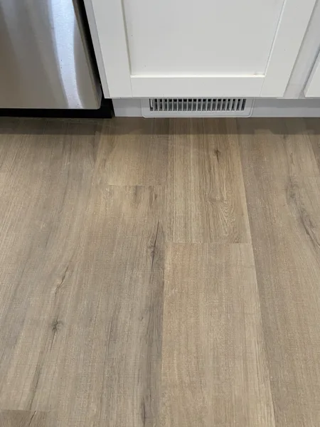 The finished plank edges around the floor vent beside the door.