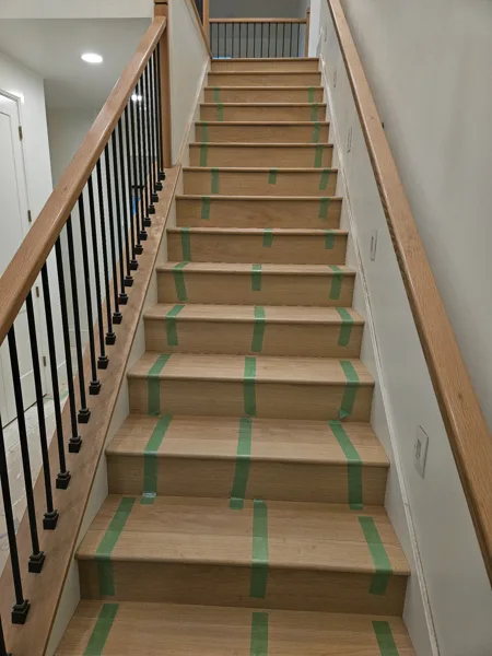 The green tape holds the stair nosing tightly against the planks while the glue sets, helping keep the joint snug and aligned.