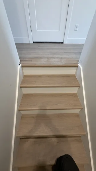 Neatly fitted tread edges carry the wood-look finish up to the doorway, connecting the stairs with the upper landing.